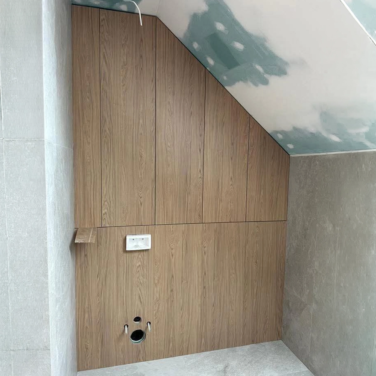 Badschrank nach Maß unter einer Dachschräge während der Montage: Fronten in Holzdekor folgen der Dachneigung und verkleiden zugleich die Vorwandinstallation des WCs.